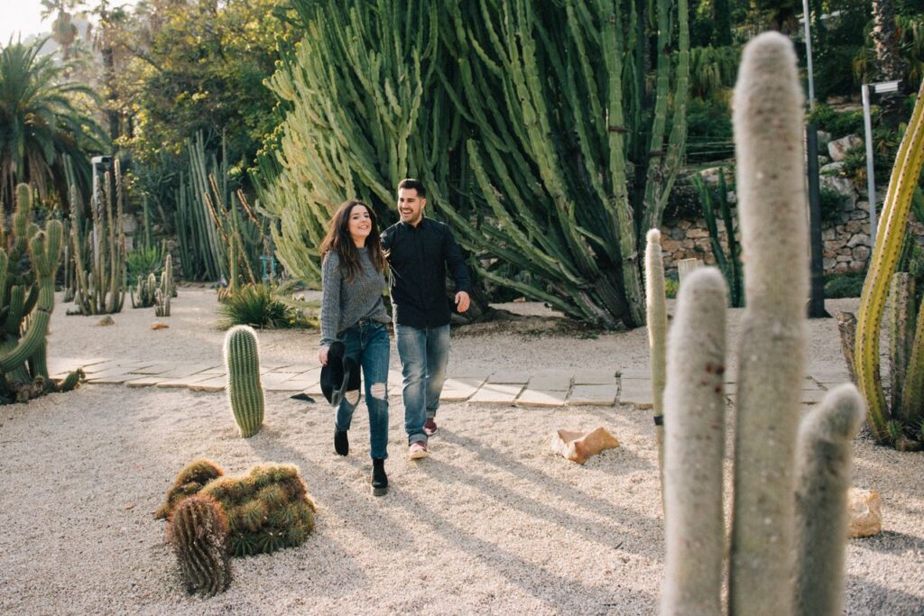 A joyful couple walks through a scenic cactus garden enjoying a sunny day.